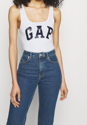 Hvid ærmeløs bodysuit med sort "GAP" logo, parret med højttaljede blå jeans. Denim har klassiske lommer og lige snit.