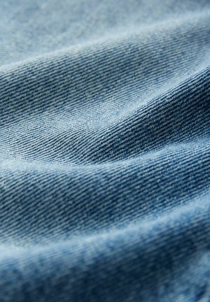 Jasnoniebieska tkanina dżinsowa o gładkiej teksturze, ukazująca drobne sploty i subtelne różnice w kolorze na powierzchni.