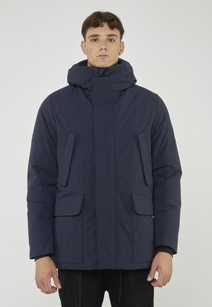 Giacca imbottita blu navy con colletto alto e cappuccio removibile. Presenta due tasche frontali e una chiusura con zip anteriore, realizzata in materiale resistente all'acqua.