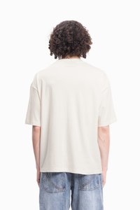 Korte mouw beige katoenen t-shirt met een relaxte pasvorm. Heeft een ronde hals en rechte zoom, gedragen met lichtblauwe denim shorts.