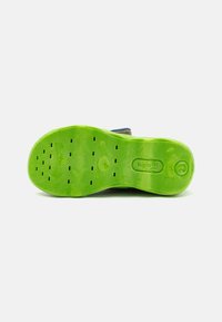 Green rubber shoe sole featuring a textured surface with drainage holes and embossed logo. Smooth edges with a slight curvature.