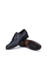 Scarpe eleganti in pelle nera con finitura liscia, cinque asole per i lacci e una suola in gomma con un motivo testurizzato.