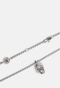 Collana in argento con pendente a forma di cranio lucido, dotata di chiusura a morsetto e dettagli con charm circolare personalizzato.