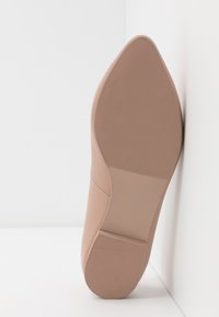 Chaussure à talon haut de couleur rose nude avec un bout pointu et une surface en cuir lisse. La semelle présente des rainures horizontales pour une meilleure adhérence et stabilité.