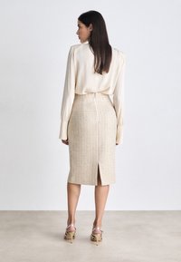 Cremefarvet bluse med lange ærmer, der er sat sammen med en pencilskirt i en tekstureret beige stof, som har en slids bagpå, samt beige hæle.