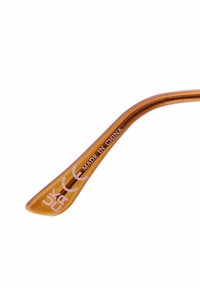 Bras de lunettes en plastique ambre décoloré avec une texture lisse, présentant du texte imprimé : "FABRIQUÉ EN CHINE" et des marquages UKCA près de l'extrémité.