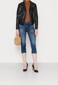 Černá kožená motocyklová bunda, hnědý žebrovaný rolák, tmavé cropped džíny, černé vysoké podpatky, s tkanou slámovou kabelkou.