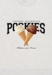 Grå genser med to iskremkjeks, en med hvit iskrem og en med brun. Teksten over og under lyder "POCKIES" og "Medioker siden alltid."