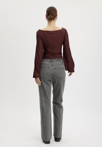 Maglione a maniche lunghe color bordeaux con scollatura ampia, abbinato a jeans grigi a vita alta con tasche posteriori e vestibilità rilassata.