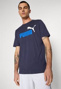 Navy blue cotton t-shirt featuring a white Puma logo and blue text. Short sleeves and a standard fit, with visible tattoos on the arm.