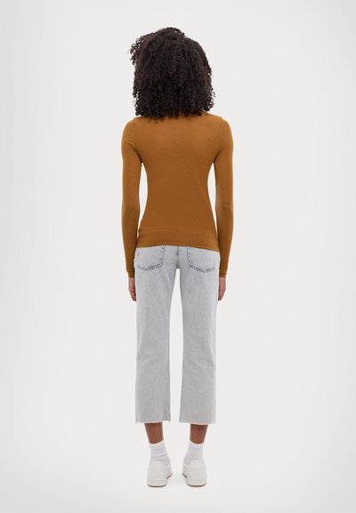 Langärmliges, figurbetontes braunes Strickoberteil kombiniert mit hellgrauen, cropped Jeans. Weiße Sneaker mit hellgrauen Sohlen. Glatte Textur.