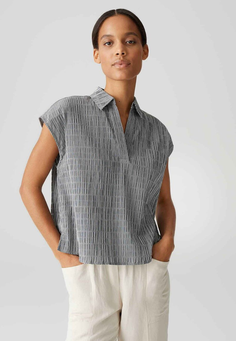 Camicia a maniche corte a righe con colletto, caratterizzata da linee verticali in colori scuri e chiari, tessuto leggero e vestibilità rilassata.