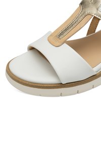 Sandalo in pelle bianca con una fascia ampia, accentato in oro e una suola spessa. Presenta una soletta testurizzata e un fondo in sughero naturale.