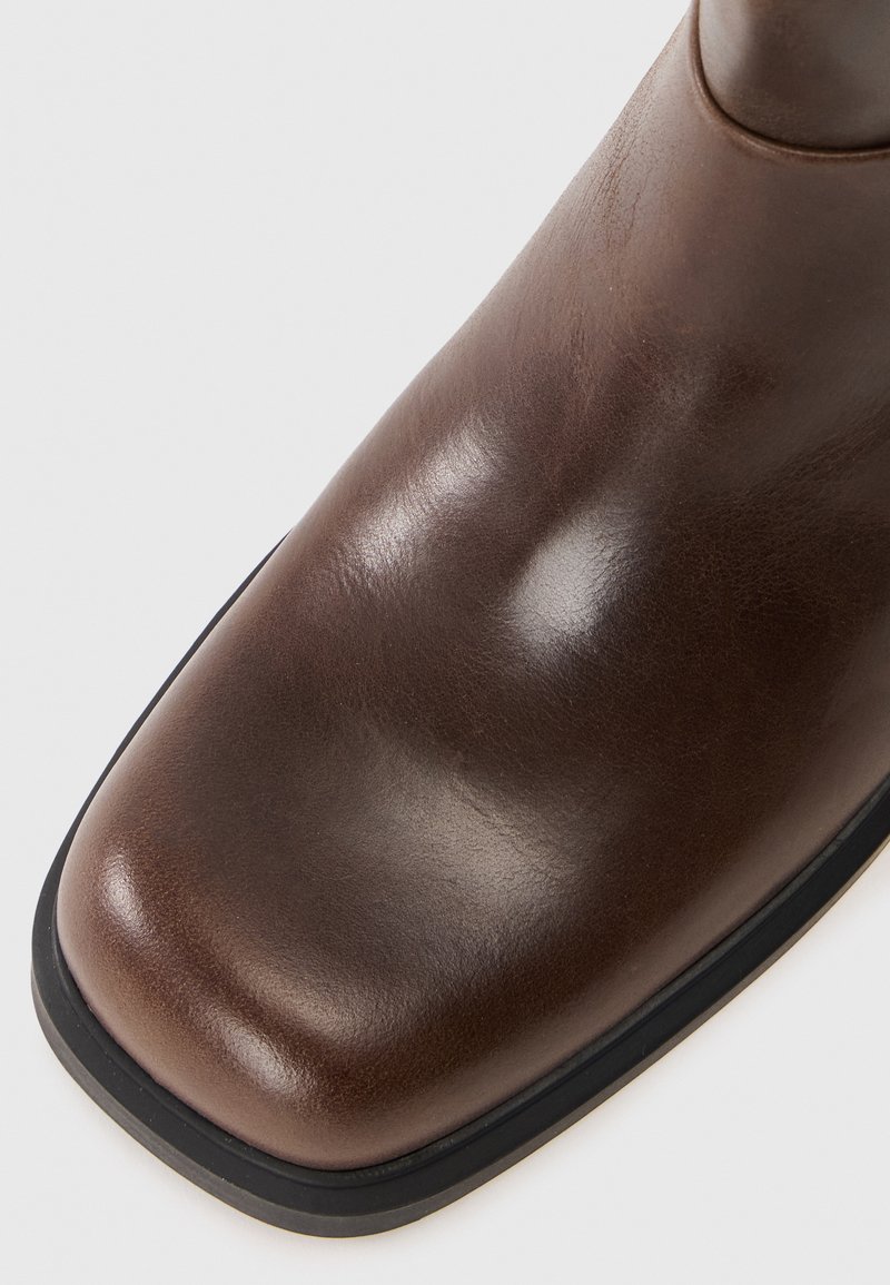 Brązowy skórzany botek za kostkę z lśniącym wykończeniem, kwadratowym noskiem i kontrastującą czarną gumową podeszwą. Prosty design z gładką teksturą.