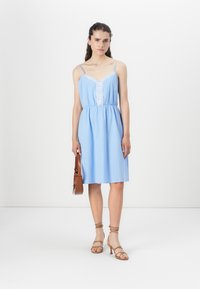 Light blue dress with spaghetti straps, v-neckline, and lace detailing at the front. Elastic waist, mid-length, paired with tan heeled sandals.