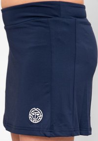 Falda de tenis azul marino hecha de tela elástica, con un ajuste ceñido y un logo blanco en el dobladillo. Textura suave.