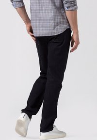Pantalones vaqueros oscuros de corte ajustado, con un diseño de bolsillo tradicional y costuras en contraste, combinados con una camisa de cuadros y zapatillas blancas.