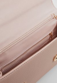 Interiér světle růžové kabelky z umělé kůže s kapsou na zip, strukturovaným povrchem, hladkou podšívkou a doplňky ve zlaté barvě.