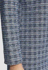 Tissu tricoté bleu et blanc avec un motif texturé, présentant des lignes horizontales et des nuances variées créant un aspect subtil et en couches.