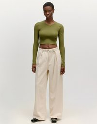 Olivgrünes, kurz geschnittenes Langarmoberteil, kombiniert mit beigen, weiten Hosen. Das Outfit zeichnet sich durch eine glatte Textur und ein minimalistisches Design aus.