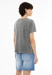 Camiseta gris de manga corta con un corte relajado. La tela parece suave con una textura sutil. Combinada con pantalones cortos de mezclilla azul claro con un dobladillo deshilachado.