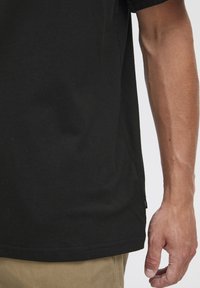 Sort bomulds T-shirt med korte ærmer, lige snit og sideslidsdetaljer. Stoffet er glat med en ensartet tekstur.