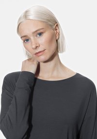 Długi rękaw bluzka w ciemnoszarym materiale o luźnym kroju i szerokim dekolcie. Gładka tekstura i minimalna ilość szwów.