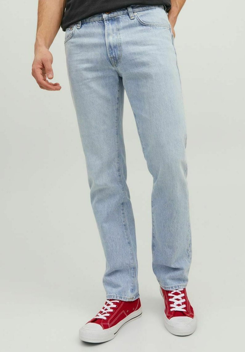 Vaqueros de mezclilla azul claro con ajuste recto, que presentan un ligero desgaste, cinco bolsillos y combinados con zapatillas rojas con detalles en blanco.