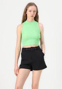 Grønn ribbede uten ermer crop topp kombinert med høyt liv svart shorts med en tykk belte, sidelommer og glidelåsdetalj.