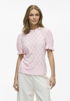 Lyserød bluse med broderi i ærmerne og scallop-udskæring, der har et tekstureret mønster af små huller over det hele.