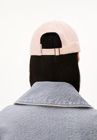 Lichtroze katoenen pet met verstelbare band aan de achterkant, gedragen met een spijkerjack van blauw denim met een uitgesneden kraag en gestructureerde stof.