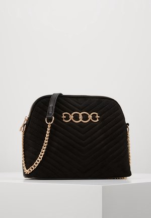 Black quilted handbag with a gold chain strap and a gold decorative circular link detail on the front.
