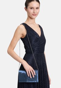 Sac à main en métal bleu avec une surface texturée, présentant un design rabattu et une chaîne décorative. Idéal pour les occasions formelles.