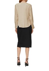 Beige satijnen blouse met lange mouwen, achteraan afgeronde zoom, gecombineerd met een zwarte pencil skirt en zwarte sandalen met hoge hakken.