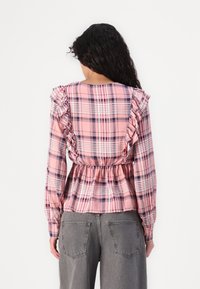 Pink plaid blouse with ruffled shoulders, cinched waist, and long sleeves. Fabric has a smooth texture with varying grid patterns.