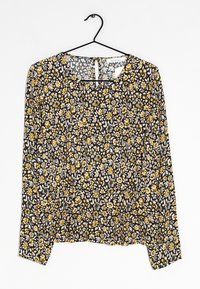Blouse noire à motifs floraux avec manches longues, motifs de fleurs jaunes et blanches, col rond et détail de ourlet froncé. Matériau en coton, texture légère.