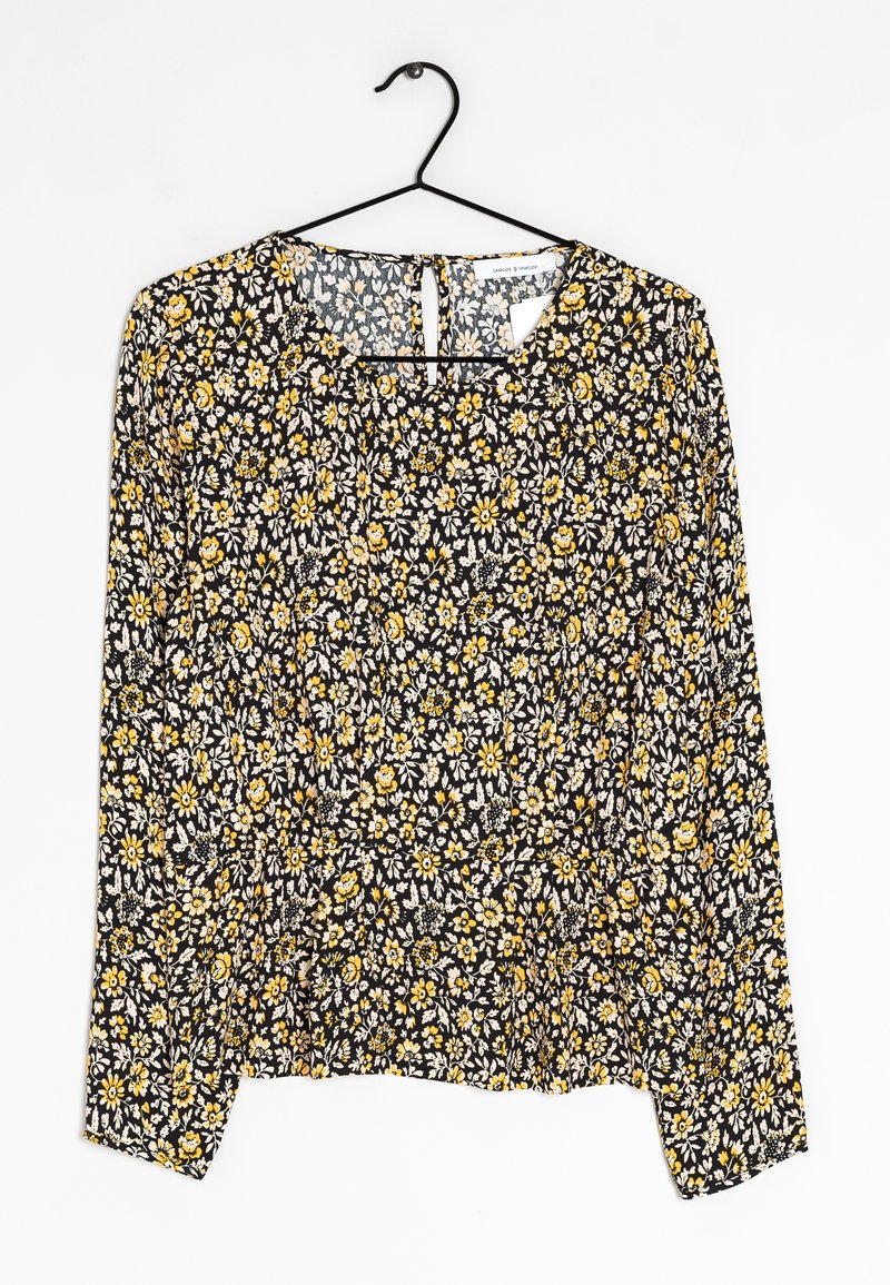 Blouse noire à motifs floraux avec manches longues, motifs de fleurs jaunes et blanches, col rond et détail de ourlet froncé. Matériau en coton, texture légère.