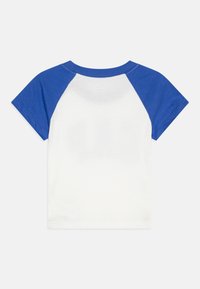 Hvit t-skjorte med blå raglanermser. Korte ermer, rund hals, laget av bomull. Glatt tekstur, klassisk snitt. Ingen synlige logoer eller mønstre.
