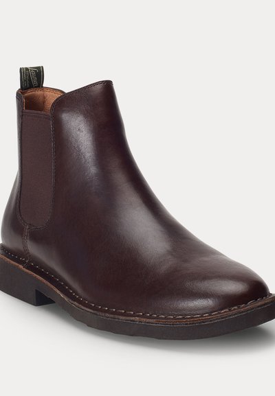 Stivale Chelsea in pelle marrone scuro con pannelli laterali elastici, linguetta sul tallone e suola cucita su sfondo chiaro.