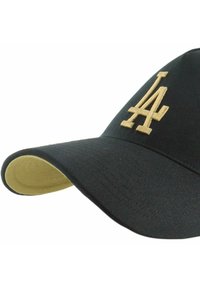 Gorra negra de tela texturizada, con un logo dorado bordado en el frente y una visera inferior amarilla contrastante.