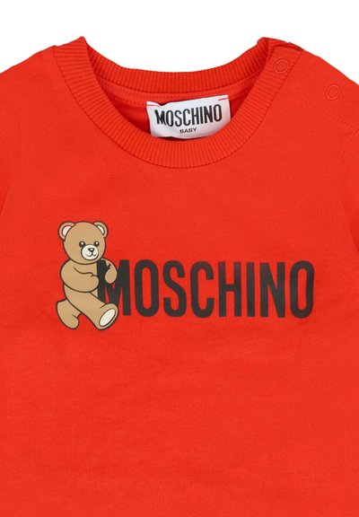 Rood babyshirt met zwarte tekst "MOSCHINO" en een beige teddybeer grafiek die de letter "M" vasthoudt op de voorkraag met drukknoopsluiting.