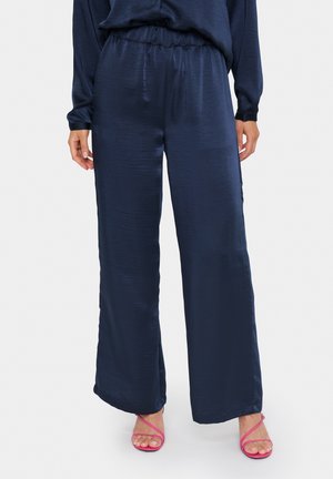 Marineblaue, weit geschnittene Hosen aus einem glänzenden, glatten Stoff mit einem elastischen Bund. Kombiniert mit rosa Riemchensandalen.