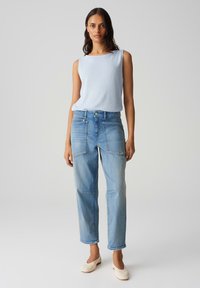 Lichtblauw mouwloos topje met een gestructureerde afwerking, gecombineerd met hoogwaisted, losvallende lichtgewassen denim jeans met voorzakken en naden.