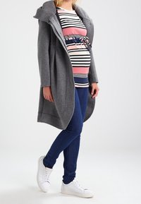 Grå lång kappa med stor huva, bärs över en rosa och navy randig topp, matchad med blå skinny jeans och vita sneakers.