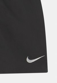 Melnas sporta bikses, kas izgatavotas no gludas auduma, ar metāliski sudraba Nike Swoosh logotipu kreisajā apakšējā stūrī.