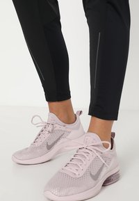 Černé sportovní legíny s reflexními detaily, spojené se světlými růžovými síťovými teniskami s šedým swoosh a polstrovanou podrážkou.