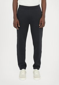 Black sweatpants with a drawstring waist, tapered leg, soft texture, and side pockets, paired with light-colored sneakers.