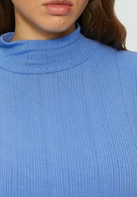 Geribbelde, lichtblauwe turtleneck top met een hoge kraag en een gestructureerde stof, die verticale lijnen over het oppervlak accentueert.