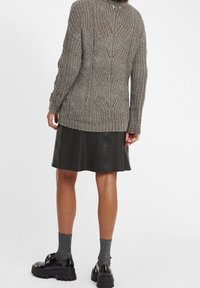 Teksturowany szary sweter dzianinowy o luźnym kroju, z wzorzystym nadrukiem i długim tylnym brzegiem, zestawiony z czarną skórzaną spódnicą.