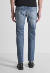 Jeans de mezclilla azul claro con un acabado desgastado, cinco bolsillos, corte recto y una cinturilla resistente, combinados con zapatos negros.